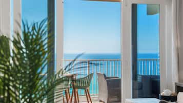 Un balcon avec vue sur la mer, une table, des chaises et une plante en pot.