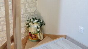 Quarto com parede de pedra, escada de madeira e uma pequena mesa com um objeto decorativo.