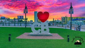 Een sculptuur met een hart en de letters 'CB', in een park met een stadsgezicht op de achtergrond.