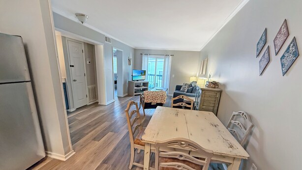 Een ruime woonkamer met een houten eettafel en stoelen, een keuken met een koelkast, en een televisie op de achtergrond.