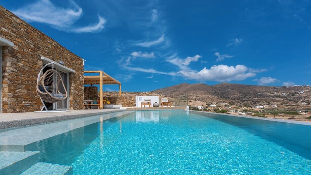A clear blue pool with a stone wall on one side and a wooden pergola with a hanging chair. - Calma Ios (Ios)