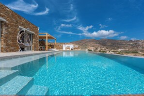 Une piscine d’un bleu éclatant, bordée d’un côté par un mur de pierre et, de l’autre, par une pergola en bois sur laquelle est suspendu un fauteuil.
