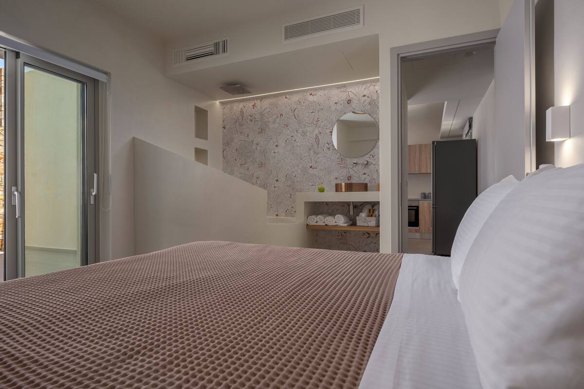 Un dormitorio moderno con una cama grande, un armario empotrado, un espejo y un baño visible a través de una puerta abierta.