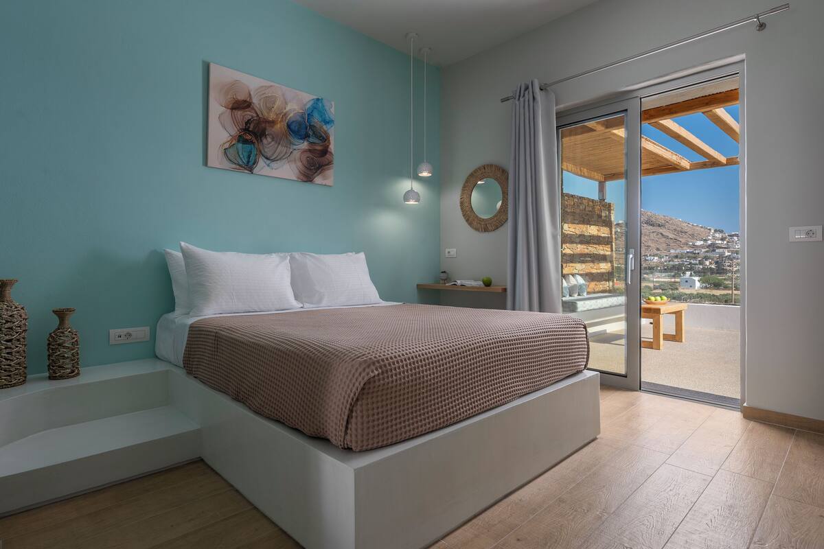 Un dormitorio con una cama, un cuadro, un espejo y vistas a un balcón con mesa y sillas.