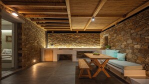 A cozy interior with a stone wall, wooden ceiling beams, a bench, and a sofa. - Calma Ios (Ios)