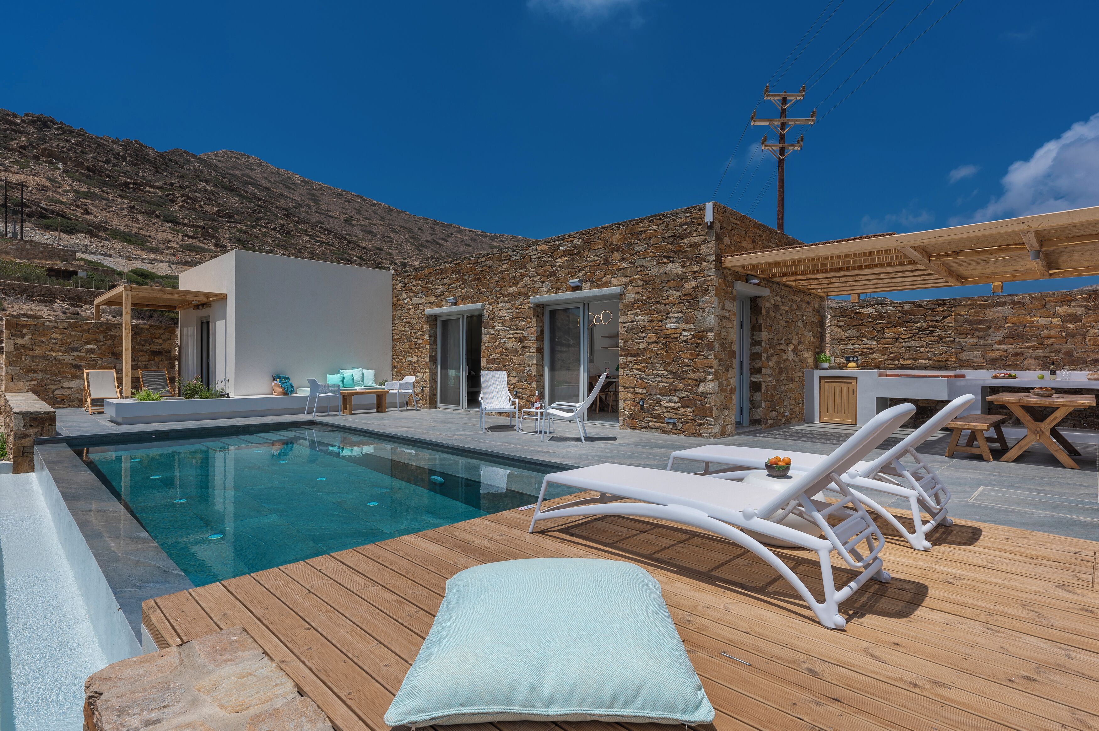 A poolside area with lounge chairs, a wooden deck, and a stone building.