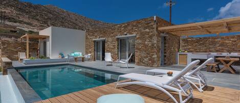 A poolside area with lounge chairs, a wooden deck, and a stone building.