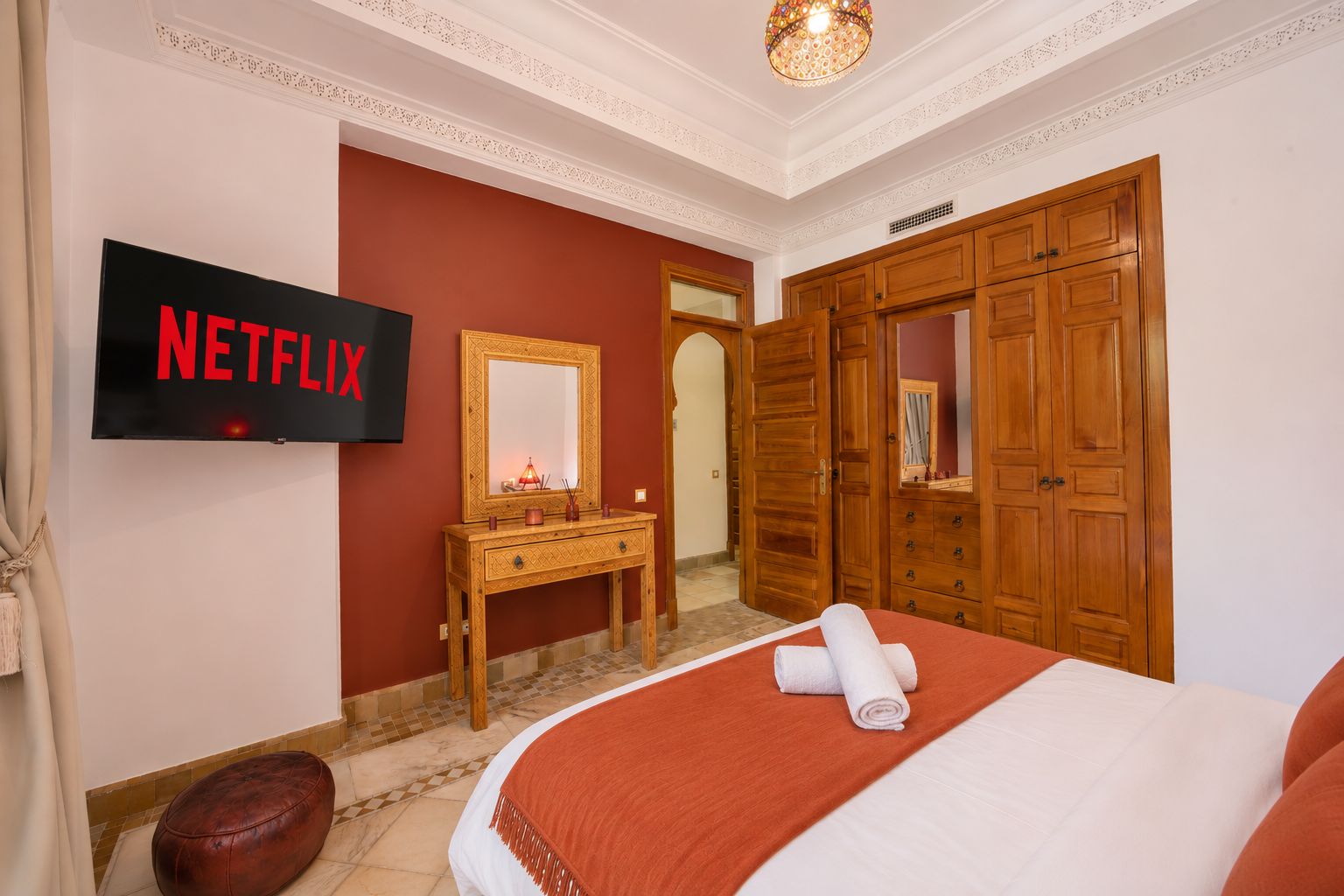 Una habitación de hotel con una cama, un armario de madera, una tocador con espejo, un televisor montado en la pared y una pared de acento roja.
