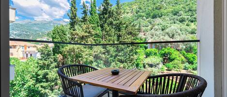 A balcony with a table and chairs, overlooking a lush green landscape with trees and a mountain in the distance.