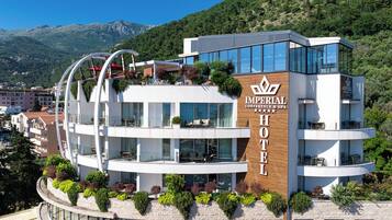 A multi-story hotel with a modern design, featuring balconies with plants, large windows, and a sign indicating it is an Imperial Conference & Spa hotel.