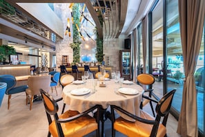 Un restaurante con techo alto, vigas a la vista y una zona de bar. Las mesas están dispuestas con manteles blancos y sillas naranjas.