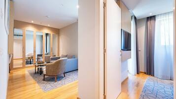 Een moderne hotelkamer met een houten vloer, een bank, een stoel, een televisie en een deur naar een andere kamer.