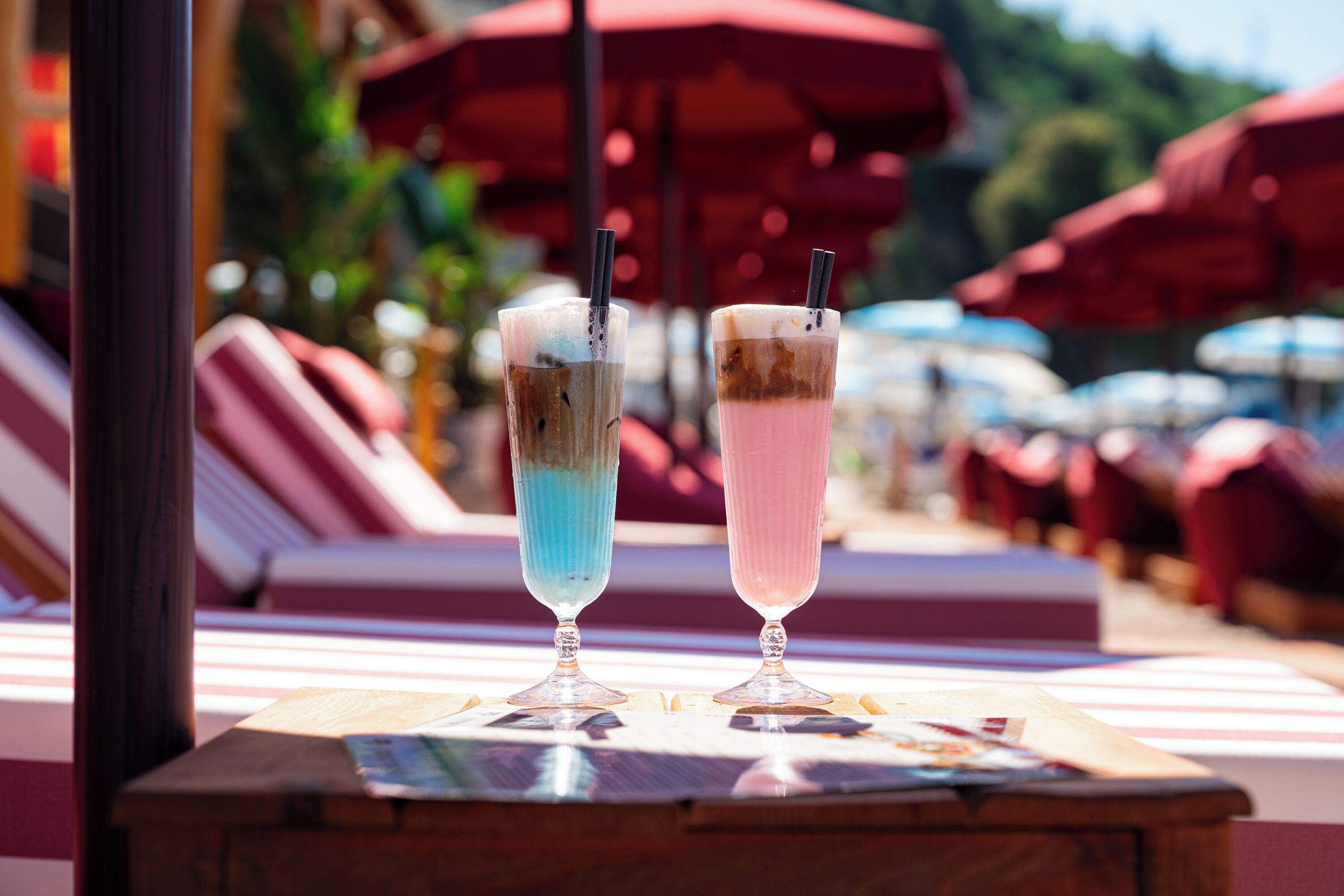 Deux boissons sur une table, accompagnées d’un magazine, entourée de fauteuils et de parasols.