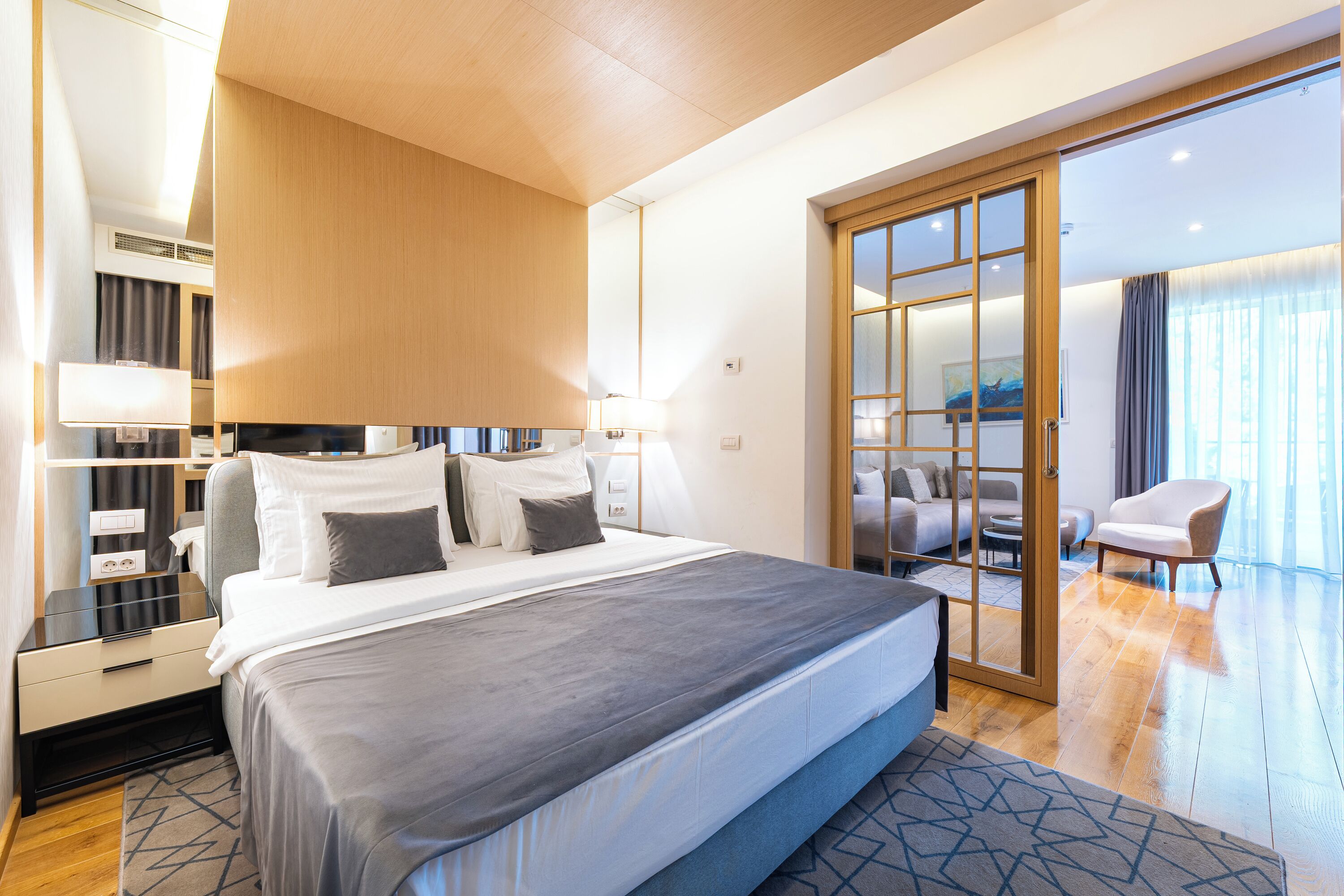 Una habitación de hotel moderna con una cama grande, un escritorio, una silla y un gran ventanal corredero que da a un balcón.