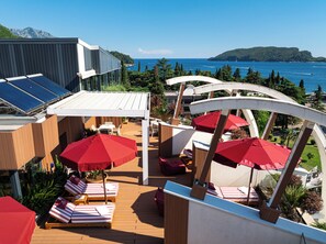 Eine Dachterrasse mit Liegestühlen, roten Sonnenschirmen und Solaranlagen.