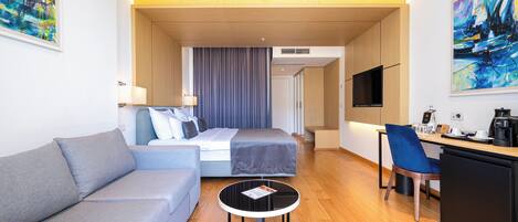 A modern hotel room with a sofa, bed, desk, chair, and a television.