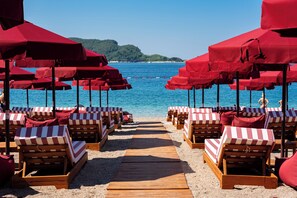 Una playa con hileras de sillas de madera y sombrillas rojas, que se extienden hasta el mar.
