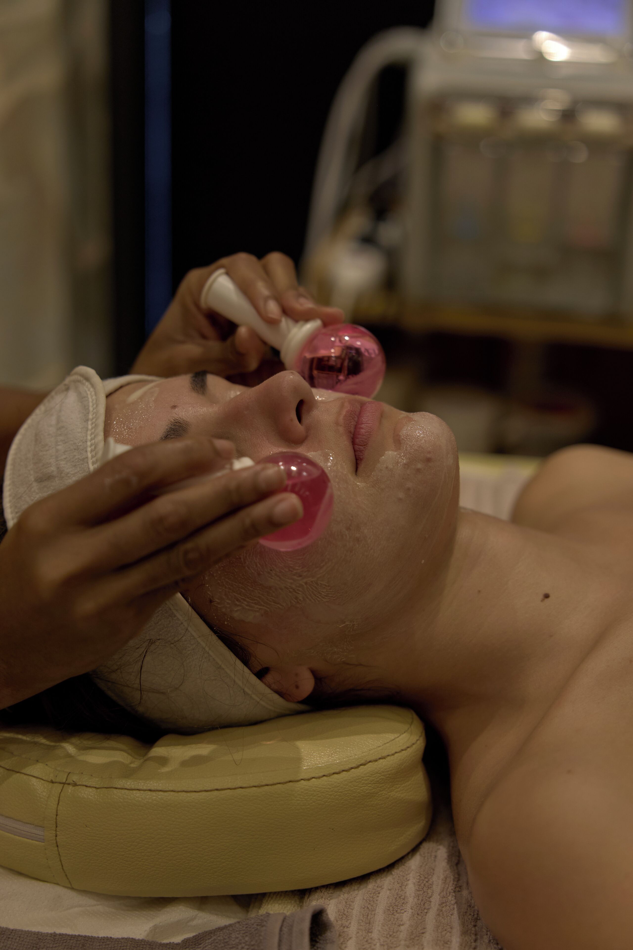 A person lying on a bed with a pillow, a white headband, and a medical device in the background.