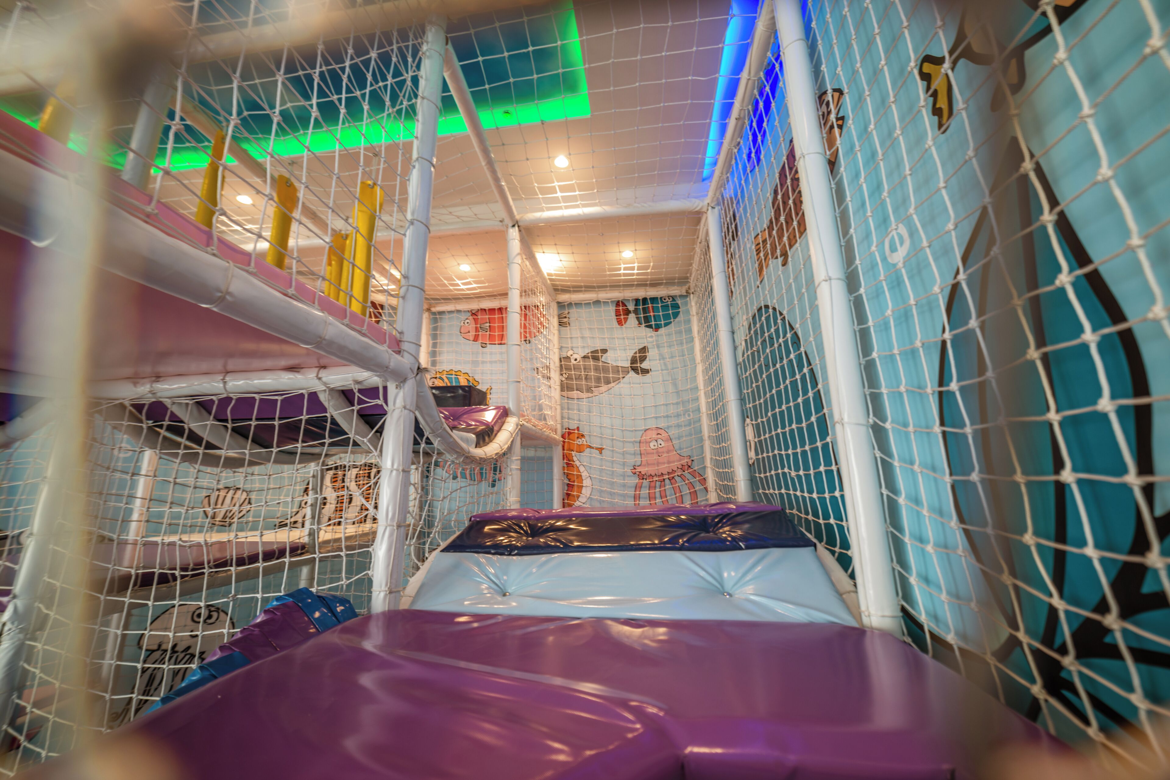 An indoor play area with a slide, netted walls, and colorful decorations.
