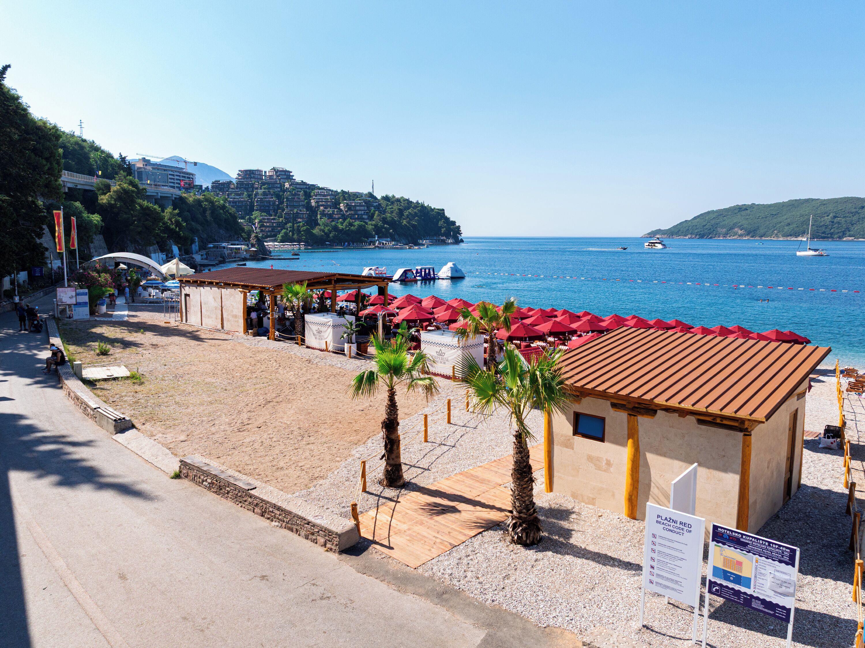 A beachside restaurant with outdoor seating, a view of the sea, and a sign indicating beach access.