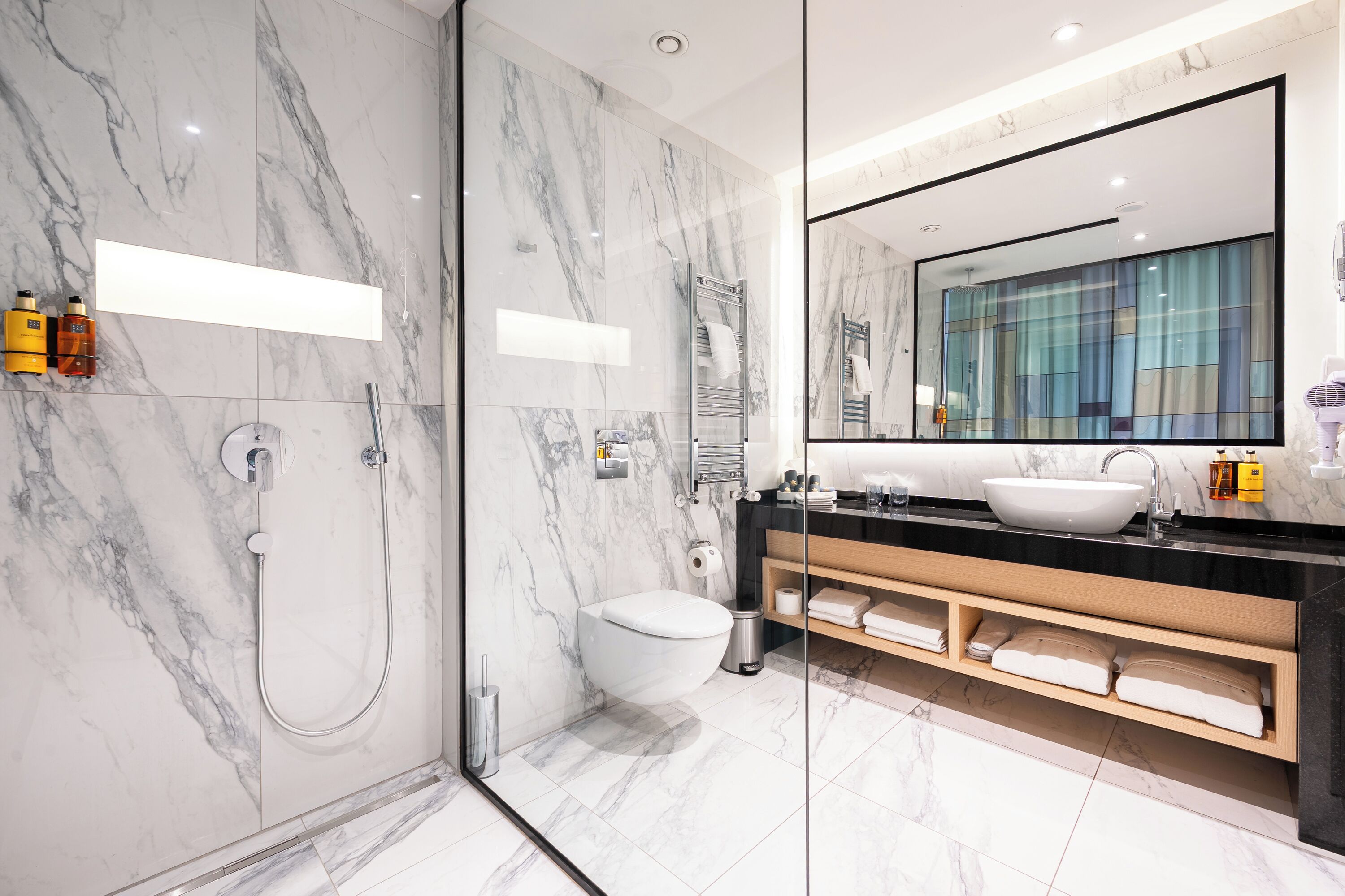 Un bagno moderno con box doccia in vetro, un water bianco, un mobile lavabo e uno specchio grande.