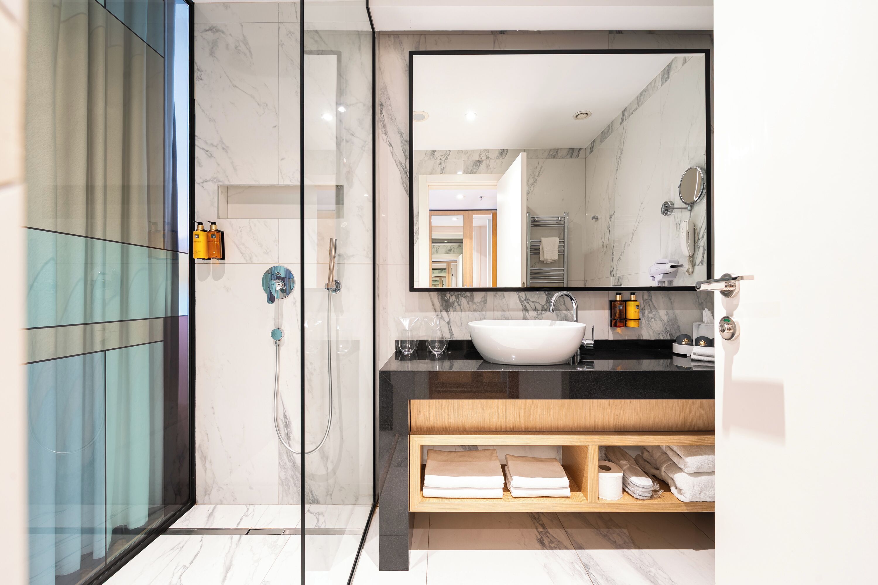 Un baño moderno con cabina de ducha de vidrio, un espejo grande y un tocador con azulejos de mármol.