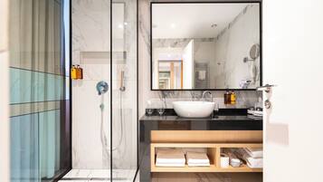 A modern bathroom with a glass shower enclosure, a large mirror, and a marble-tiled vanity.