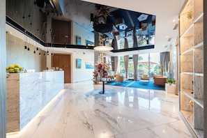 A modern hotel lobby with a marble reception desk, a staircase, and a large TV screen. - Hotel Imperial Conference & Spa (Budva)