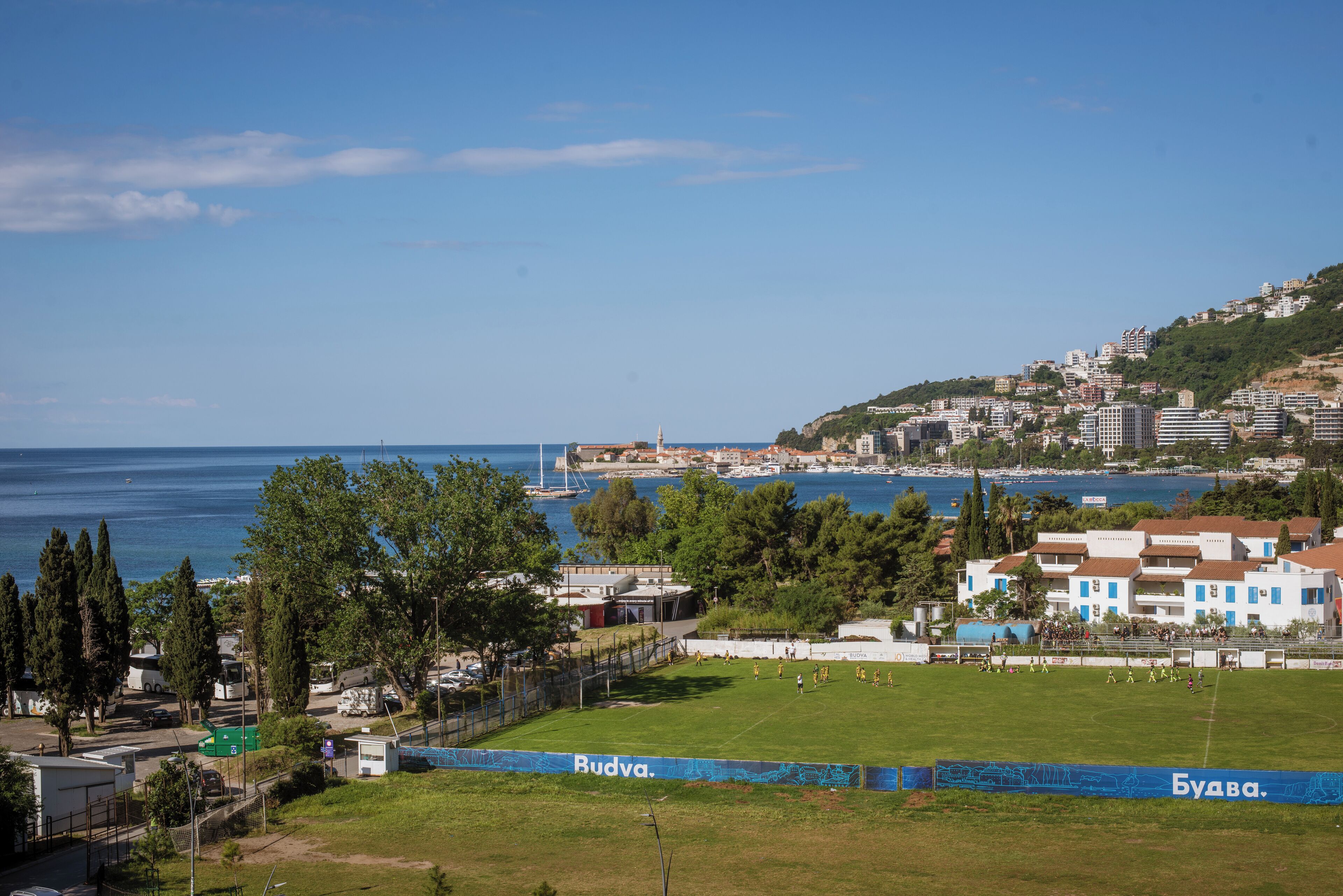 A coastal view with a grassy field, a clear sky, and a distant cityscape.