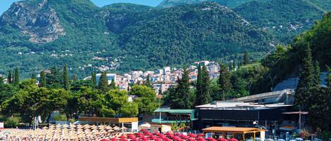 Une station balnéaire dotée de parasols, de chaises longues et offrant une vue sur une ville et des montagnes en arrière-plan.