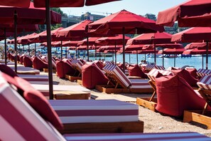 A beach with rows of wooden lounge chairs and red umbrellas.