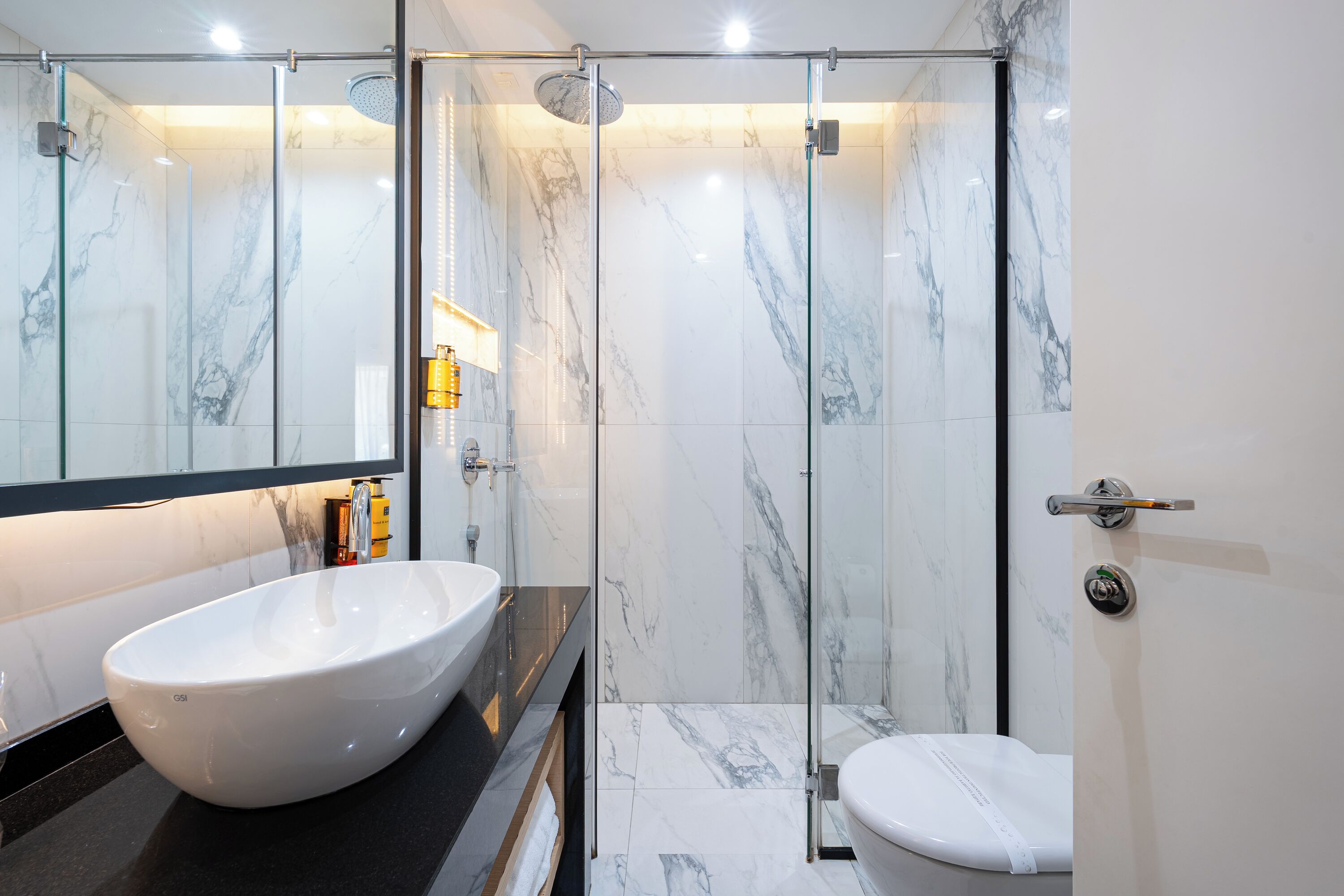 A modern bathroom with a large white vessel sink, a glass-enclosed shower, and a toilet.