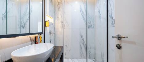 A modern bathroom with a large white vessel sink, a glass-enclosed shower, and a toilet.