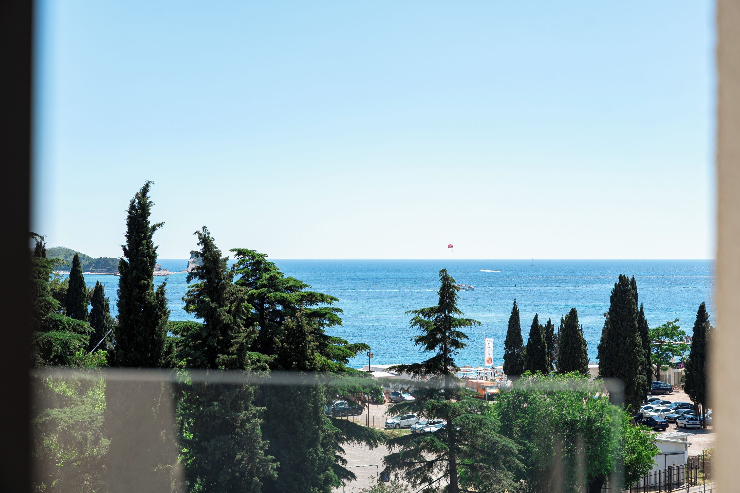A coastal view with trees, parked cars, and a clear sky.