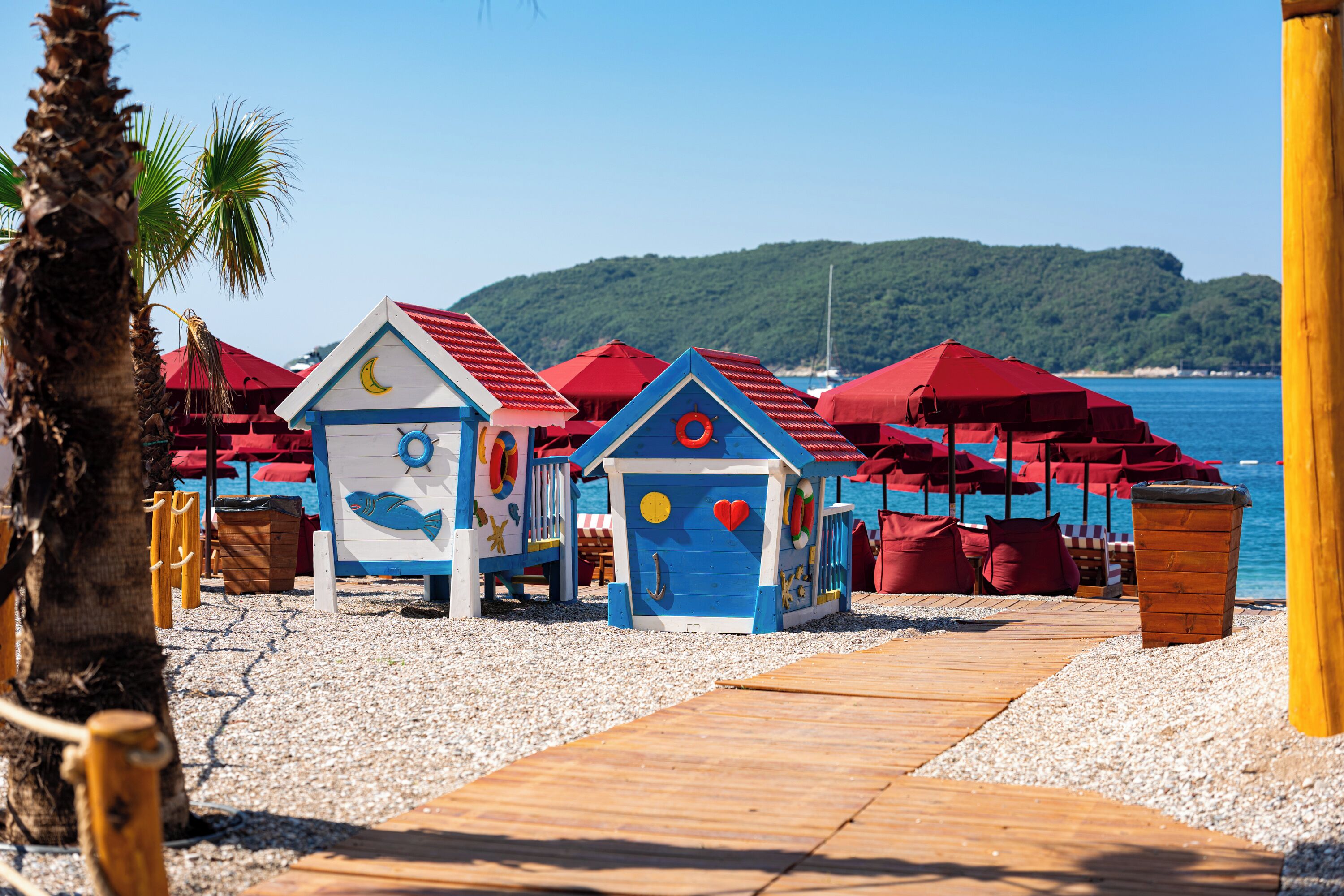 A beach with colorful beach huts and red umbrellas.