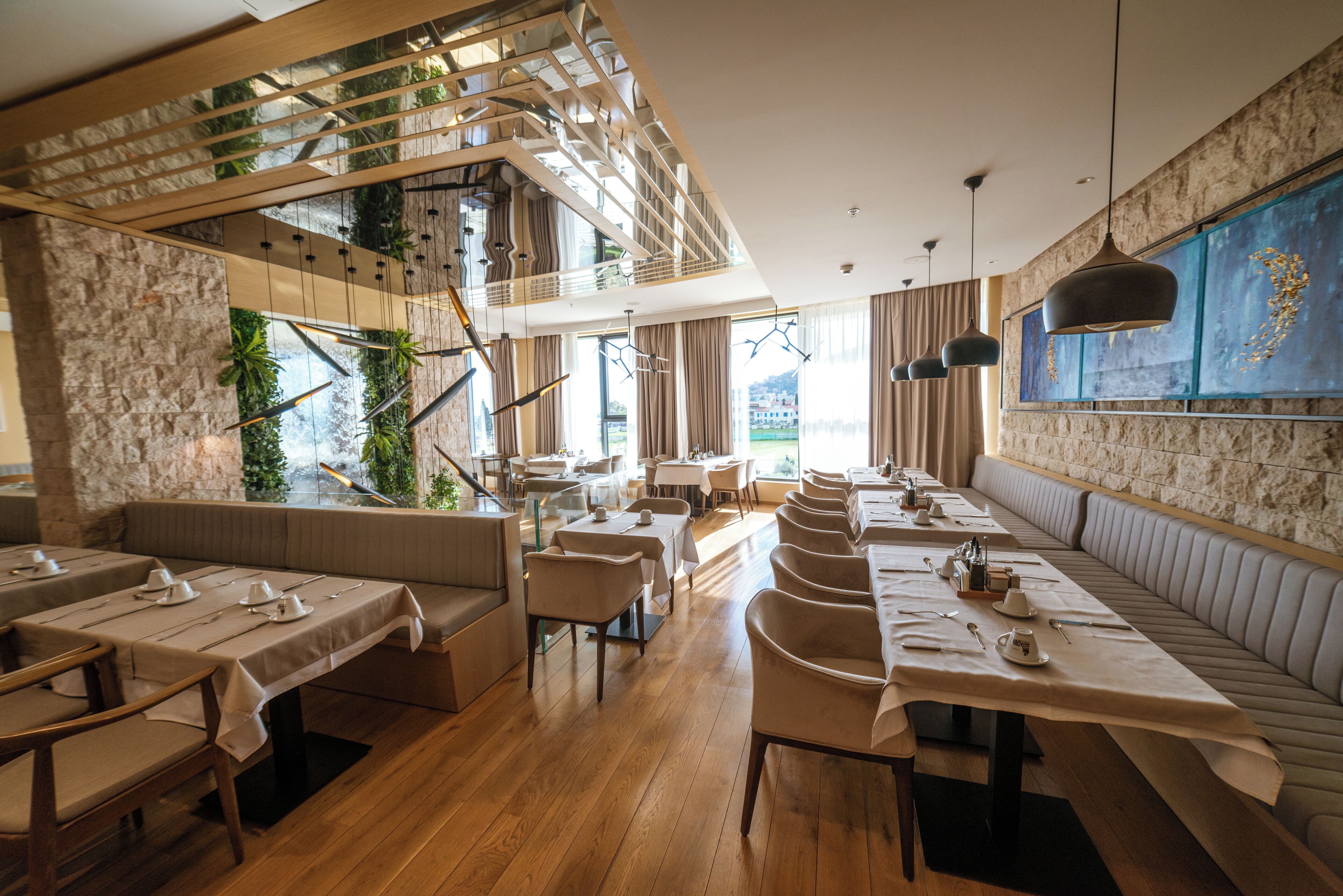 A modern restaurant with wooden flooring, multiple dining areas, and a high ceiling with exposed beams.