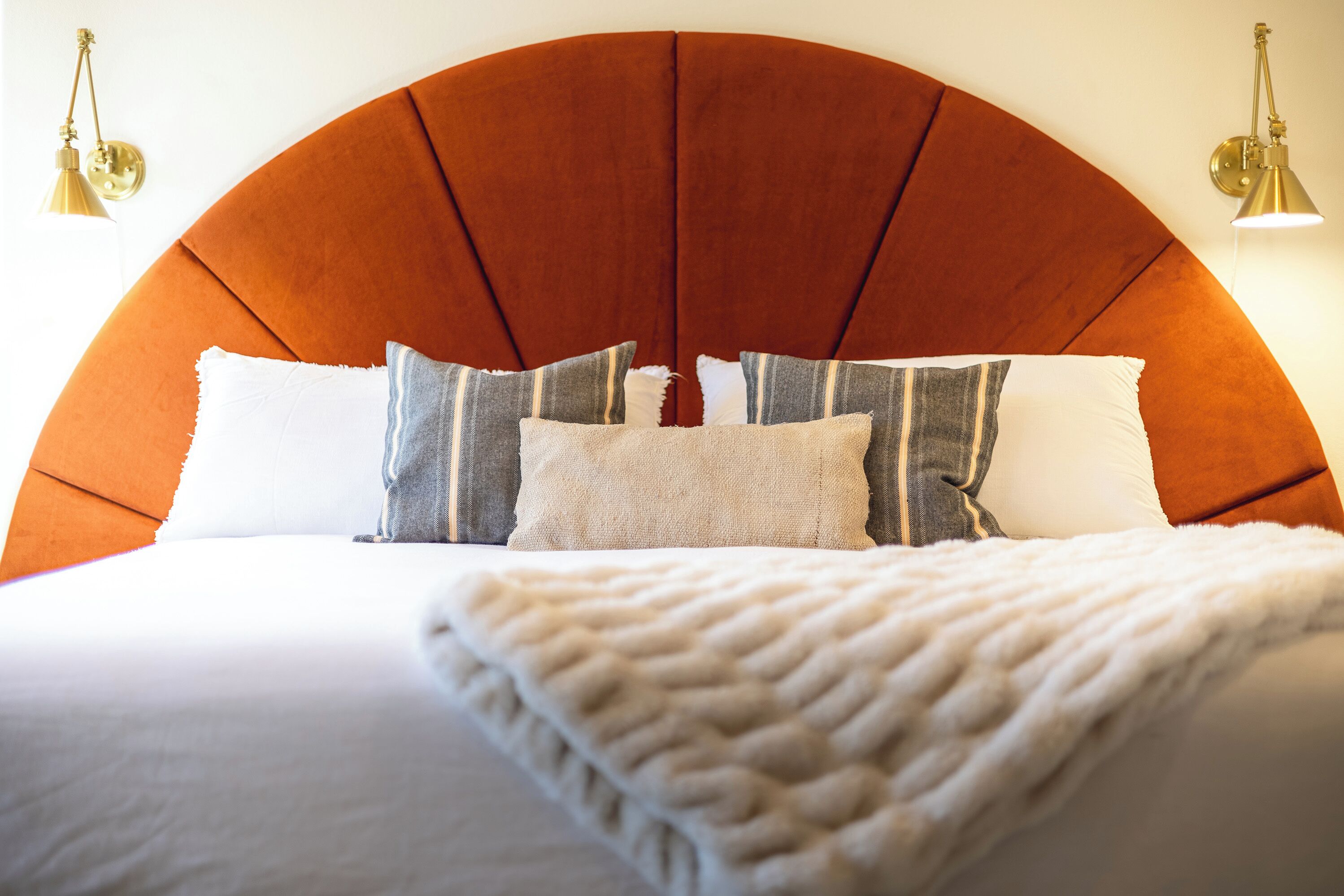 Un lit avec une tête de lit incurvée, plusieurs oreillers et une couverture blanche.