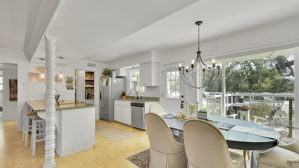 Una cocina amplia con una isla central, armarios blancos y un comedor con candelabro.