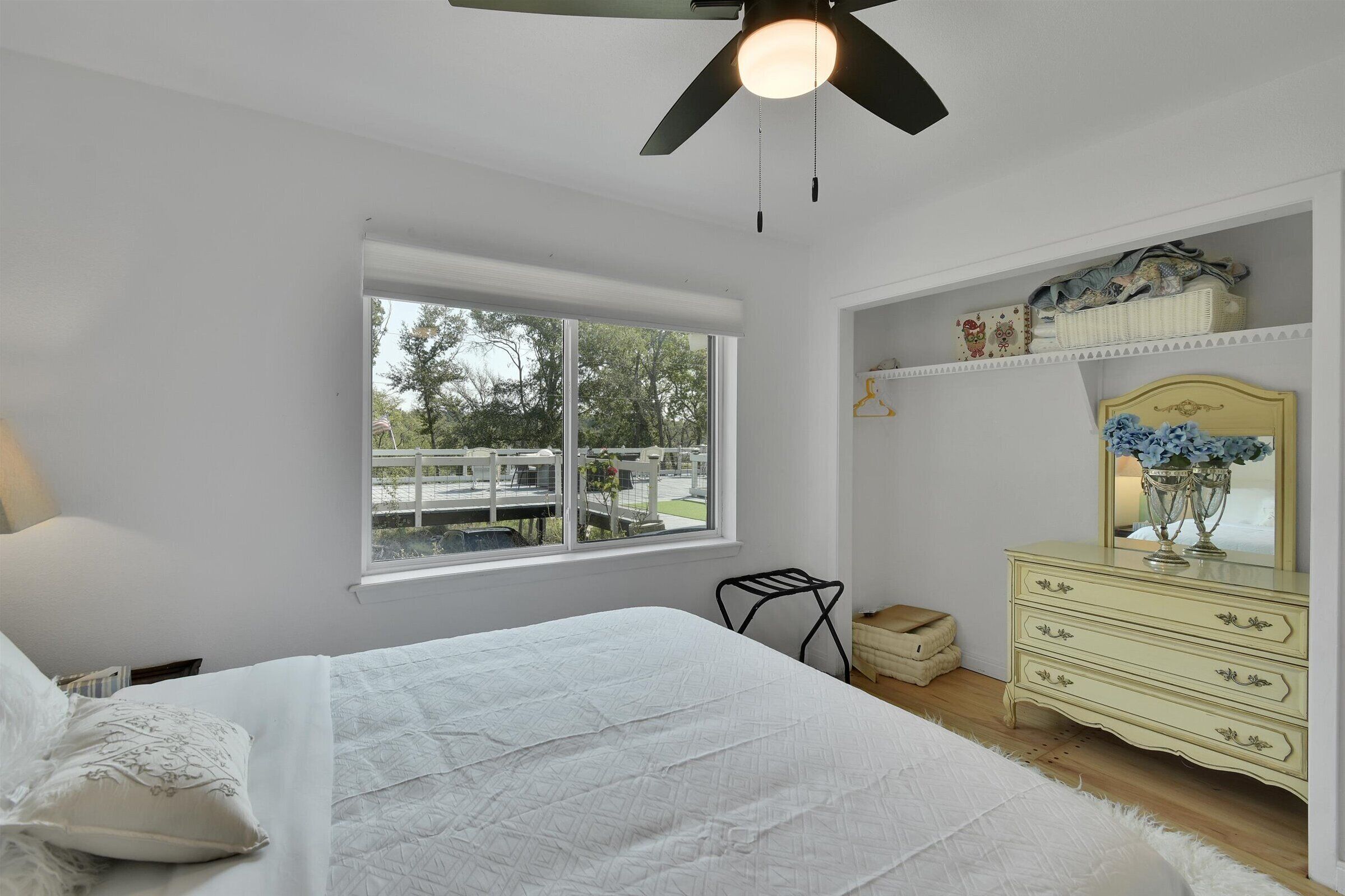 A bedroom with a bed, a dresser, a mirror, and a window with a view of a park.
