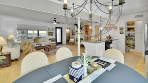 Una sala de estar moderna con una araña, una mesa de comedor y una cocina al fondo.