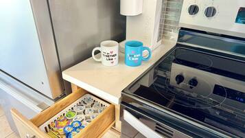 A kitchen with a coffee maker, two mugs, and a drawer with food items.