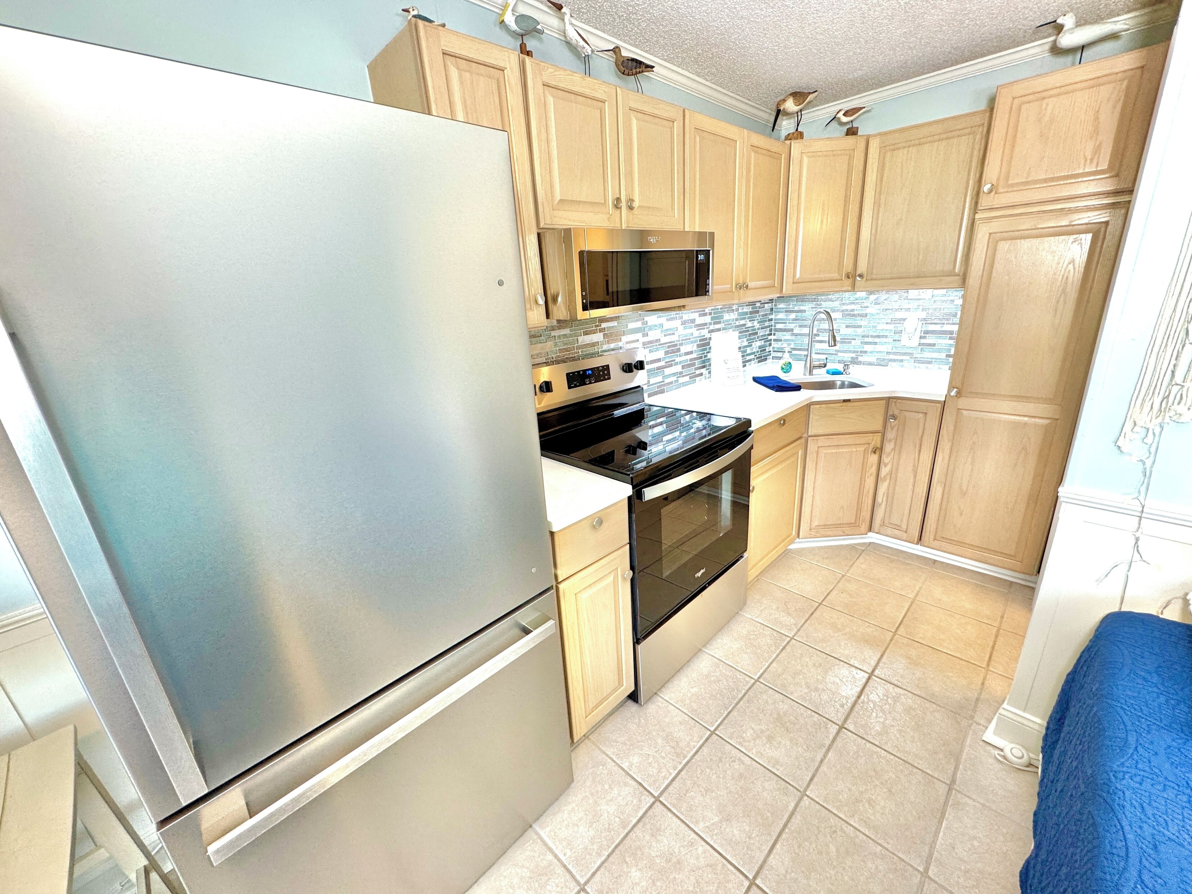 A kitchen with light wooden cabinets, stainless steel appliances, and a tiled backsplash.