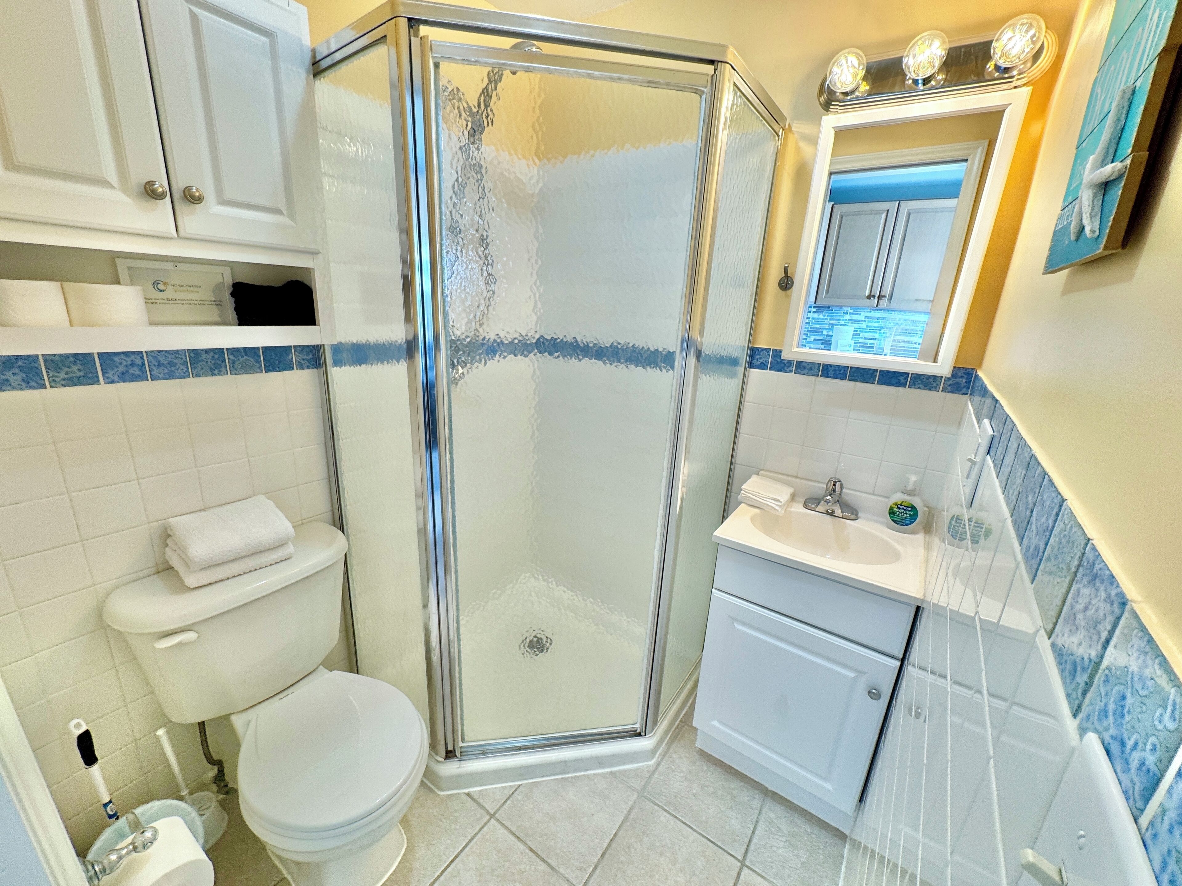 Un baño con ducha acristalada, inodoro, lavamanos y espejo.