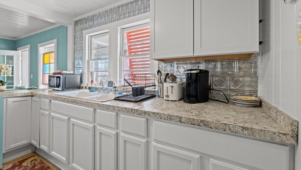 A kitchen with white cabinets, a granite countertop, and a window with red blinds. - High Tide in Windy Hill (North Myrtle Beach)