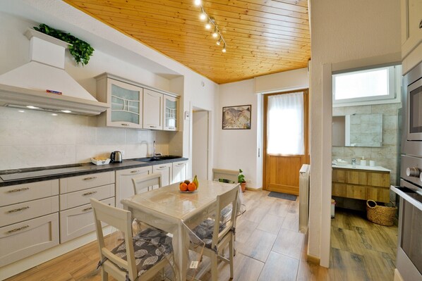 A modern kitchen with white cabinets, a dining table with chairs, a radiator, and a window with curtains.