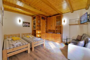 A room with two wooden beds, a sofa, wooden cabinets, and a television.