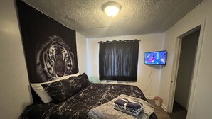 Une chambre à coucher avec un lit, un téléviseur fixé au mur, un luminaire au plafond et une porte.