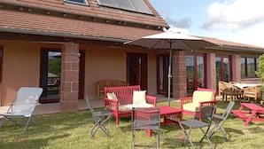 Een huis met een terras, meubels en een grote parasol.