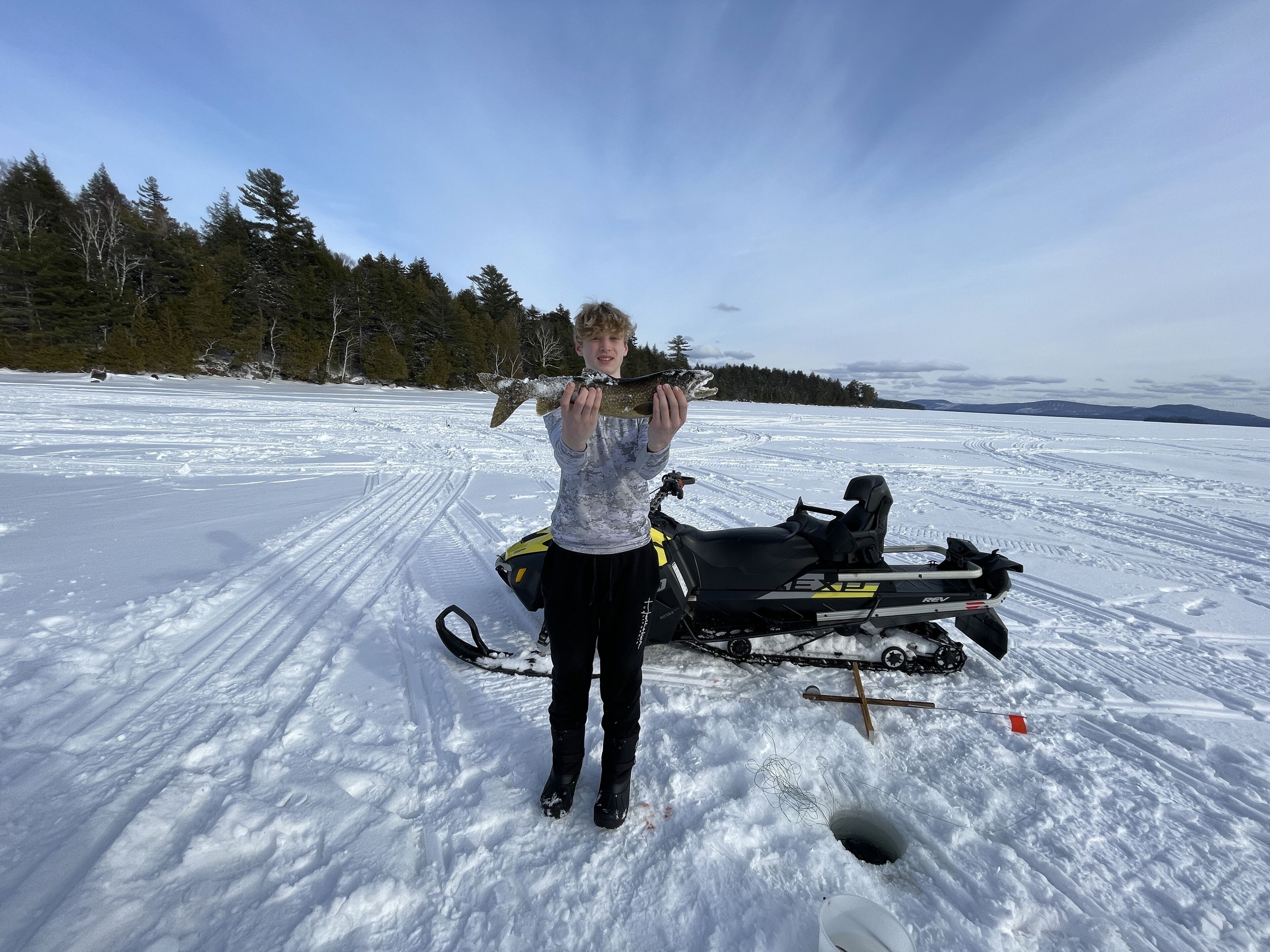 A person standing on a snowy field with a snowmobile and a fish.