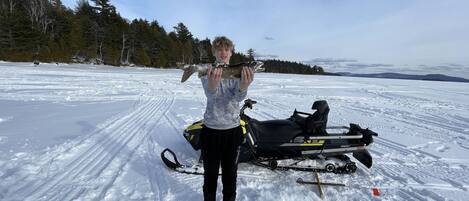 A person standing on a snowy field with a snowmobile and a fish.